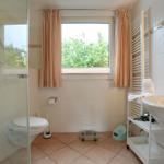 Badezimmer mit Dusche, Toilette, Waschbecken und Fenster mit Vorhängen.