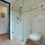 Badezimmer mit Dusche, Toilette und Blick in Schlafzimmer.