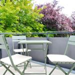Terrasse mit grünem Tisch und drei Stühlen, Blick auf Bäume.
