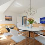 Wohn- und Essbereich mit runden Tisch, weißen Stühlen und gelbem Sofa unter schrägen Decken.