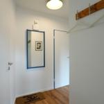 Eingangsbereich mit Spiegel, Holzboden und Kleiderhaken an der Wand.
