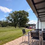 Terrasse mit Tisch und Stühlen. Blick auf grünes Feld und Baum.