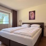 Schlafzimmer mit Doppelbett, Fenster und Wandbild.