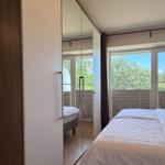 Schlafzimmer mit Doppelbett, Spiegelschrank und Blick auf Balkon mit Bäumen.