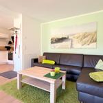 Wohnzimmer mit Sofa, Couchtisch und Küchenbereich. Wandbild zeigt Strand.