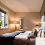 Schlafzimmer mit Bett, Nachttisch, Stehlampe und Fenster mit Pflanze.