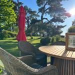 Terrasse mit Rattanmöbeln, Holztisch und rotem Sonnenschirm. Grüner Garten und Bäume im Hintergrund.