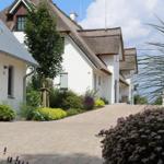 Haus mit strohgedecktem Dach und gepflastertem Weg durch Garten mit Blumen.
