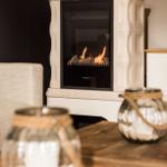 Ein Kamin mit brennendem Feuer steht im Raum. Vor ihm befindet sich ein Holztisch mit zwei Glasbehältern.