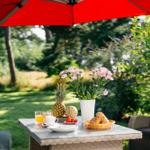 Tisch unter rotem Sonnenschirm mit Obst, Blumen und Kaffee.