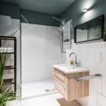Badezimmer mit Dusche, Waschbecken und Pflanzen. Wandfarbe dunkelgrau, weiße Fliesen.