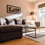 Ein Wohnzimmer mit grauem Sofa, Holztisch und Fensterblick auf Außenbereich.