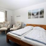 Ein Schlafzimmer mit Doppelbett, zwei Sesseln und Wandbildern.