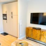 Küche mit eingebautem Ofen und Wohnbereich mit TV und Holzschrank.