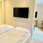 Zimmer mit Bett und Wandfernseher. Durchgang in Wohnbereich mit Tisch und Stuhl.