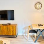 Wohn- und Essbereich mit Holztisch, Stühlen, Fernseher und Wanduhr.