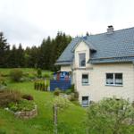 Haus mit Garten und Wald im Hintergrund. Blaue Fensterläden und Dachziegel.