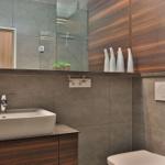 Bad mit Waschbecken, Spiegel und Holzschränken. Dusche mit Glaswand und Toilette.