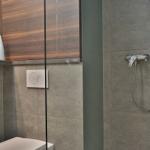 Bad mit Dusche, Toilette und Holzschränken. Graue Fliesen und weiße Keramik.