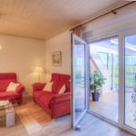Wohnzimmer mit roten Sofas, Glas-Tisch und Blick auf Terrasse mit Garten.