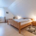 Schlafzimmer mit Holzbett, Nachttisch und Fenster mit Vorhang.