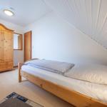 Schlafzimmer mit Holzbett, Kleiderschrank und schräger Decke.