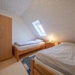 Zimmer mit zwei Betten, Schrank und Dachfenster. Holzboden und weiße Wände.