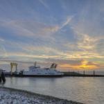 Ferries an der Hafeneinfahrt bei Sonnenuntergang mit klarem Himmel und ruhigem Wasser.