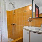 Badezimmer mit Dusche, Waschbecken und Spiegel an orangefarbenen Fliesen.