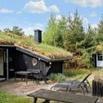 Haus mit grüner Dachdeckung, Terrasse mit Tisch, Stühlen und Liegen. Umgeben von Bäumen.