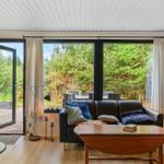 Wohnzimmer mit Sofa, Tisch und Blick auf Garten durch große Fenster.