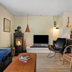 Wohnzimmer mit Kamin, Sofa, Fernseher und Stühlen. Holzboden und große Fenster.
