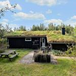 Ein dunkles Holzhaus mit grünem Dach, Garten und Picknicktisch unter blauem Himmel.
