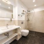 Badezimmer mit Dusche, Waschbecken und Toilette. Fliesenboden und Spiegelschrank.