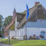 Traditionelles Haus mit Strohdach und blauer Tür. Grünflächen und Blumen vor dem Eingang.
