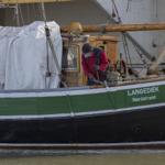 Ein Mann repariert ein altes Schiff mit der Aufschrift LANGEDIEK.