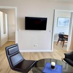 Living room with TV, two black chairs, and glass table. Doorways to bedroom and dining area.