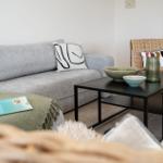 Ein grauer Sofa mit Kissen, ein schwarzer Couchtisch und ein Stuhl aus Rattan.