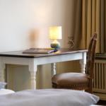 Schreibtisch mit Stuhl, Lampe und Buch neben Fenster mit Vorhängen.