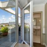 Terrasse mit Blick auf Stadt und Turm, angrenzender Badezimmerbereich mit Waschbecken.