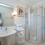 Badezimmer mit Dusche, Waschbecken und Toilette. Weiße Fliesen und goldene Accessoires.