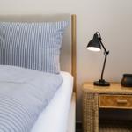 Bettkopfteil mit Kissen und Nachttisch mit Lampe und Kerze.