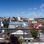Blick von Balkon auf Stadt mit Dächern und Turm unter blauem Himmel.