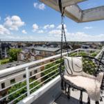 Terrasse mit Hängesessel und Stadtblick. Weiße Geländer und Dachterrassenansicht.