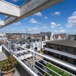 Terrasse mit Blick auf Stadt und Turm unter blauem Himmel mit weißen Wolken.