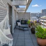 Terrasse mit Hängemöbel, Liegestuhl und Pflanzen. Blick auf Hochhäuser.