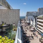 Terrasse mit Tisch und Stühlen, Blick auf belebte Straße und Meer.