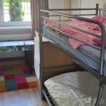 Zimmer mit Doppelstockbett, buntem Teppich und Fenster mit Blick nach draußen.