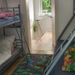 Zimmer mit Doppelstockbetten und Kinderzimmer-Teppich. Durchgang zum Flur mit Fenster.