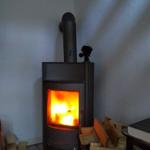 Holzofen mit brennendem Feuer, umgeben von Brennholz und einem Korb.